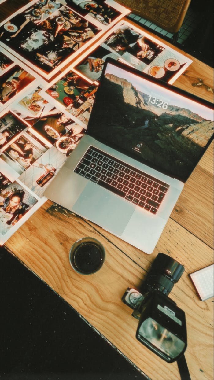 Flat lay of a creative workspace with a laptop, camera, and printed photographs.