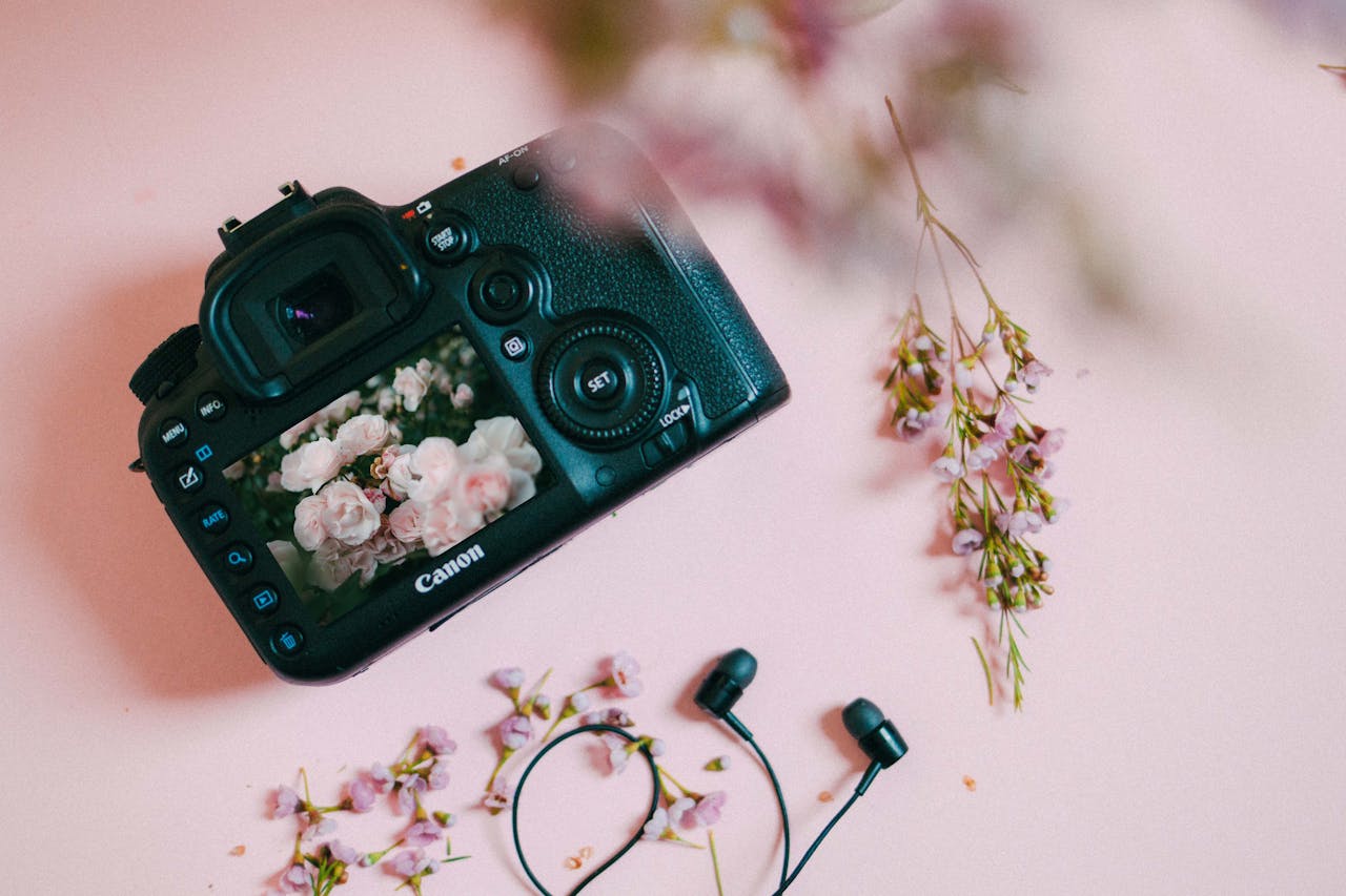Flat lay of camera with floral theme on pink with headphones.